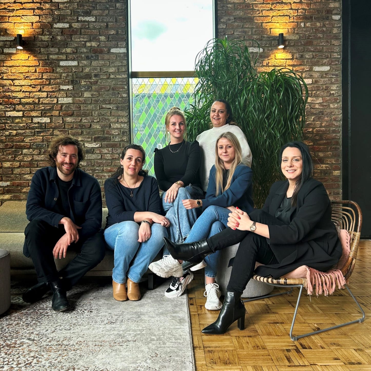 Het Exxtra-team zit samen te lachen in een zithoek met bakstenen muur en planten.