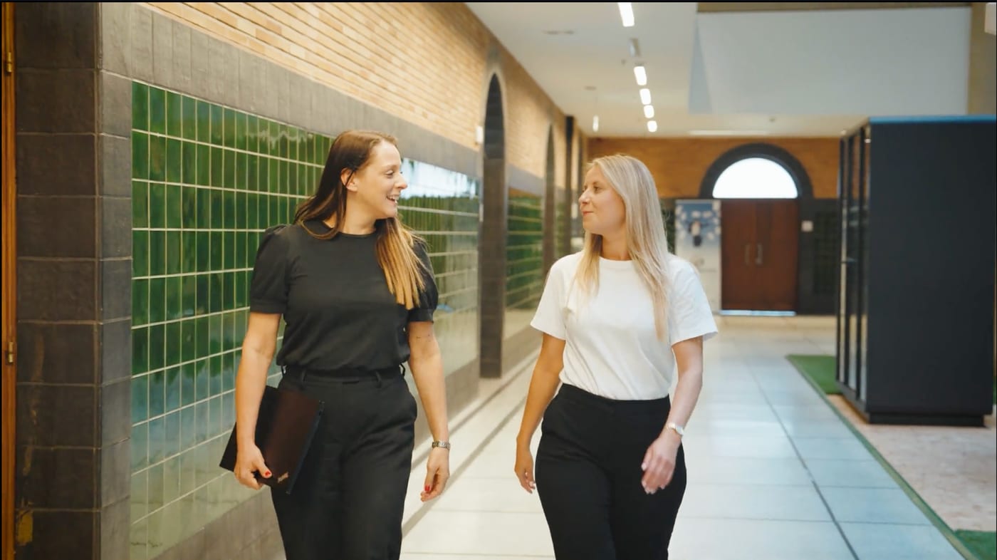 Twee vrouwen wandelen pratend door een gang.