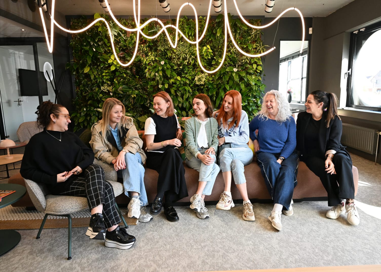 Het Exxtra-team zit samen op een bank voor een groene plantenwand.